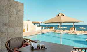 Utsikt från en altan mot en pool med parasoller och solstolar, med havet i bakgrunden. (AI-genererad text)