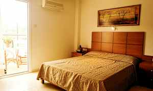 Ett sovrum med en säng, ett nattduksbord, och en tavla på väggen; bredvid finns en öppen balkongdörr. (AI-genererad text)