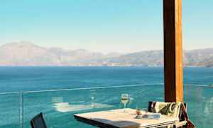 Bord och stolar vid en terrass med utsikt över havet och bergen. (AI-genererad text)