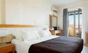 Ett hotellrum med en dubbelsäng klädd i vita lakan och ett mörkt täcke. I rummet finns också ett skrivbord med spegel och en balkong med utsikt. (AI-genererad text)