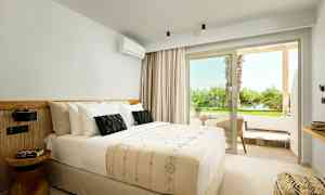 Interiör av ett ljust hotellrum med en dubbelsäng, en liten sittgrupp utanför med utsikt över grönska. (AI-genererad text)