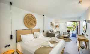 Ett modernt hotellrum med en stor säng, sittgrupp och en utsikt över en pool genom glasdörrar. (AI-genererad text)