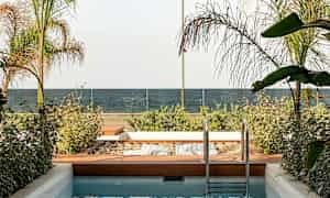 En liten pool med en träträdgård bredvid, utsikt mot ett hav och glasräcke. (AI-genererad text)