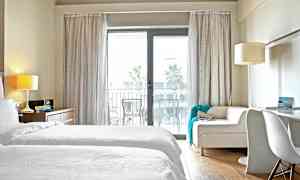 Ett hotellrum med vita sängkläder och en soffa framför en glasdörr till en balkong. (AI-genererad text)