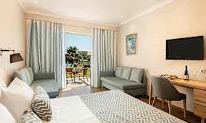 Ett hotellrum med en stor säng, sittgrupp och ett skrivbord. Uteplatsen syns genom glasdörrar. (AI-genererad text)