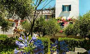 En vit byggnad med blåa fönsterluckor och blommande växter i trädgården. (AI-genererad text)