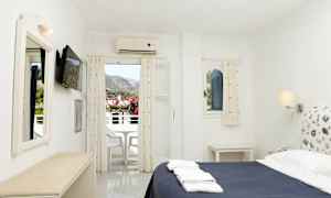 Ett hotellrum med en säng, en tv på väggen och en balkong som visar utsikt över bergen. (AI-genererad text)