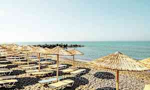 En strand med solstolar och parasoller framför ett lugnt hav. (AI-genererad text)