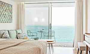 Ett sovrum med havsutsikt genom stora glasdörrar som leder till en balkong. (AI-genererad text)