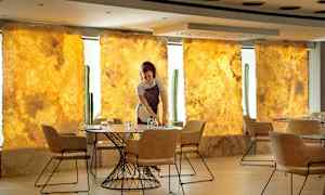 En servitör dukar ett bord i en elegant restaurang med gyllene bakgrund och moderna stolar. (AI-genererad text)