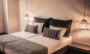 Ett sovrum med en dubbelsäng, prydnadskuddar och hängande lampor. (AI-genererad text)