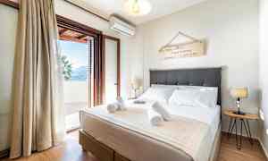 Ett sovrum med en dubbelsäng, dekorativ väggskylt, sänglampor och en öppen balkongdörr som leder ut till en terrass. (AI-genererad text)