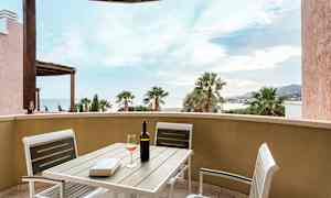 Utsikt från en terrass med bord och stolar, vinflaska och glas. (AI-genererad text)