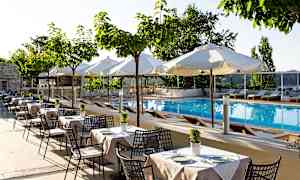 Bild av en utomhuspool med solstolar och vita parasoller, omgiven av bord och stolar under små träd. (AI-genererad text)