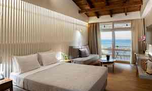 Hotellrum med dubbelsäng, soffa, och balkong med havsutsikt. (AI-genererad text)