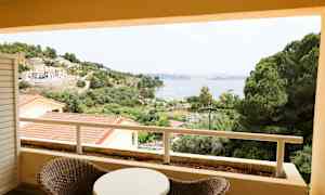 Utsikt från en balkong över grönska, byggnader och en vik. (AI-genererad text)