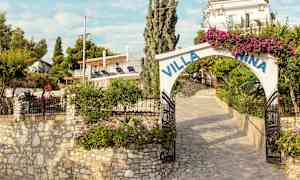 En stenlagd ingång till Villa Nina med blommor och grönt runtom. (AI-genererad text)