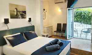 Ett hotellrum med en bäddad säng och mörkblå lakan, ett öppet fönster mot balkongen, och möbler inklusive två stolar och en byrå. (AI-genererad text)