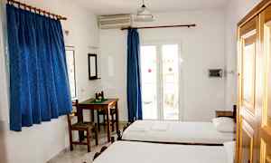 Ett hotellrum med två enkelsängar, ett bord med stolar, blå gardiner och en balkongdörr. (AI-genererad text)