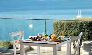 Ett dukat bord med diverse maträtter och utsikt över havet. (AI-genererad text)