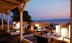 En restaurangterrass med bord och stolar vid solnedgången, havet i bakgrunden. (AI-genererad text)