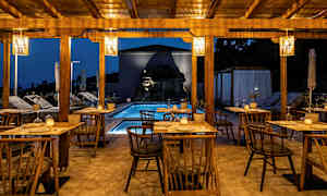 Utomhusservering med trästolar och bord, pool och belysning under kvällen. (AI-genererad text)