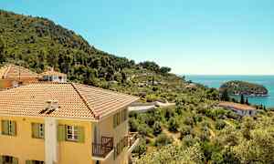 Byggnad med gult fasad och sluttningslandskap ovanpå med havsvy. (AI-genererad text)