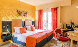 Ett hotellrum med två sängar, orange inredning och röda gardiner, samt ett mindre bord med stolar och dekorationer. (AI-genererad text)