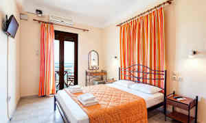 Rum med dubbelsäng, orange överkast och gardiner, en spegel och bord samt en balkongdörr. (AI-genererad text)