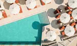 En pool med turkost vatten och omgivande solstolar under randiga parasoller. (AI-genererad text)