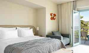 Hotelrum med bäddad säng, fåtölj och öppen balkongdörr. (AI-genererad text)