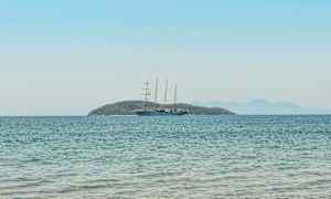 En segelbåt på öppet vatten med en ö i bakgrunden. (AI-genererad text)