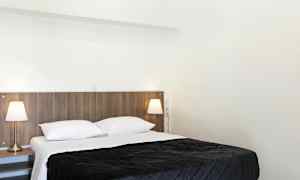 Ett sovrum med en dubbelsäng, vita sängkläder och en mörk överkast. Två sänglampor finns på sängbord bredvid sängen. (AI-genererad text)