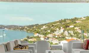 Utemöbler på en terrass med utsikt över havet och en kuststad. (AI-genererad text)