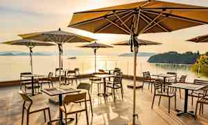 Uteservering med bord och parasoller vid havet i solnedgång. (AI-genererad text)