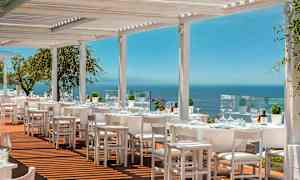 Utomhusrestaurang med vita möbler och utsikt över havet. (AI-genererad text)