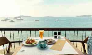 Utsikt över en tallrik med mat och en kopp kaffe placerade på ett bord med en balkong som vetter mot havet. (AI-genererad text)