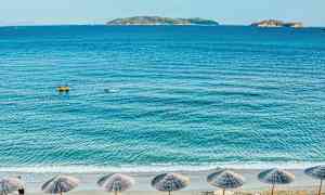 Strand med parasoller, hav, och öar i bakgrunden. (AI-genererad text)