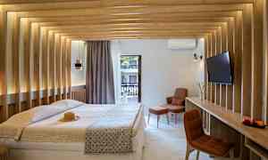 Ett modernt hotellrum med en dubbelsäng, träpaneler på väggarna, och utsikt mot en balkong. Rummet har en tv och en bekväm sittplats. (AI-genererad text)