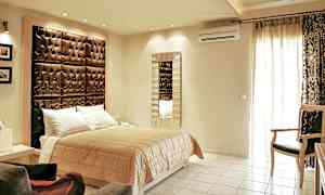 Ett sovrum med en dubbelsäng, ett stort vadderat huvudgavel och en spegel på väggen. (AI-genererad text)