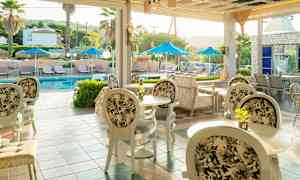 Bild på en uteservering med bord och stolar, och en pool med solstolar och parasoller i bakgrunden. (AI-genererad text)