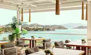 Uteservering med bord och stolar, samt utsikt över havet och grönskande öar. (AI-genererad text)