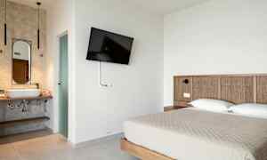 Hotellrum med en dubbelsäng, väggmonterad TV och ett öppet badrum. (AI-genererad text)