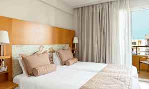 Två bäddar i ett hotellrum med ljusa textiler och trädetaljer. (AI-genererad text)