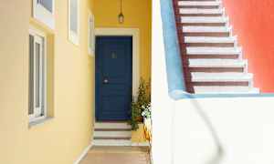 En blå dörr med steg och en gul vägg vid sidan av en trappa med rött väggparti. (AI-genererad text)