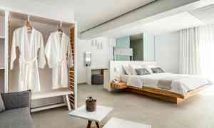 Bild av ett elegant hotellrum med en stor säng, vita badrockar hängande i en garderob och ljusa moderna möbler. (AI-genererad text)