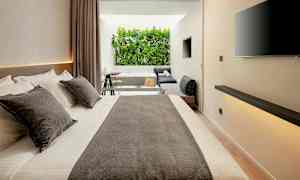 Modern hotelrum med stor säng, sittgrupp och utsikt över grönska. (AI-genererad text)