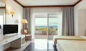 Interiör av ett hotellrum med två sängar, skrivbord och en uteplats med utsikt över havet. (AI-genererad text)