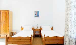 Två enkelsängar med träramar i ett ljust rum med vita väggar, en liten nattduksbord med lampa mellan dem. (AI-genererad text)