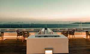 En terrass med sittplatser och bord med utsikt över havet i solnedgången. (AI-genererad text)